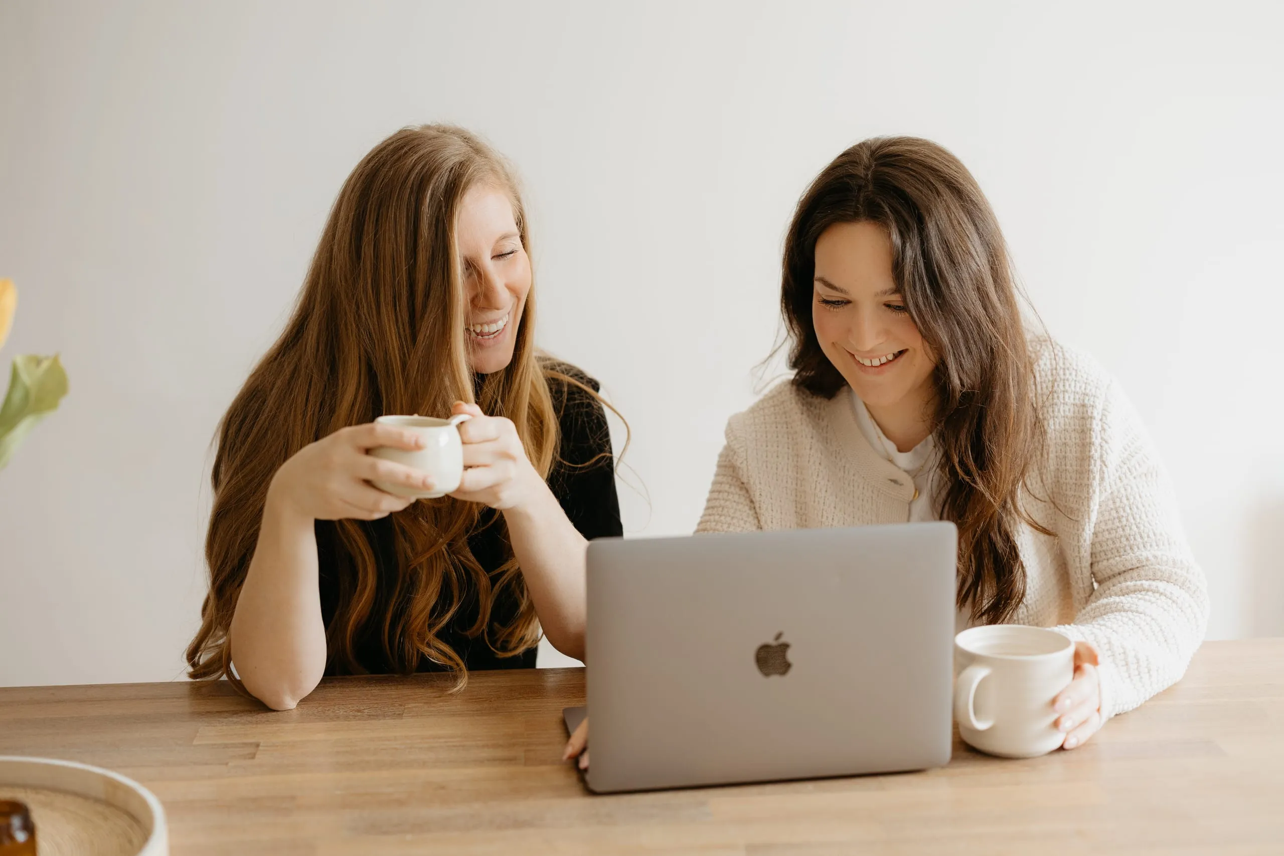 Daphné et Vicki souriantes devant un portable, tasses de café en main